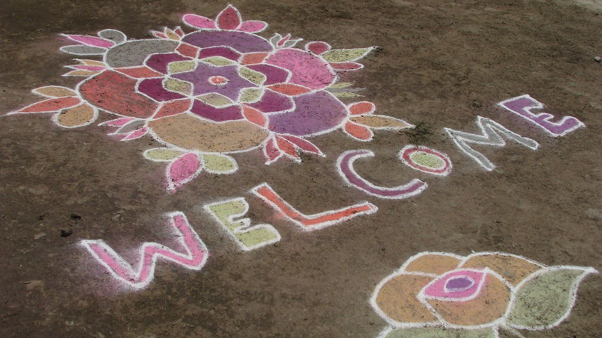 A colourful kolam drawn on the ground with the word Welcome
